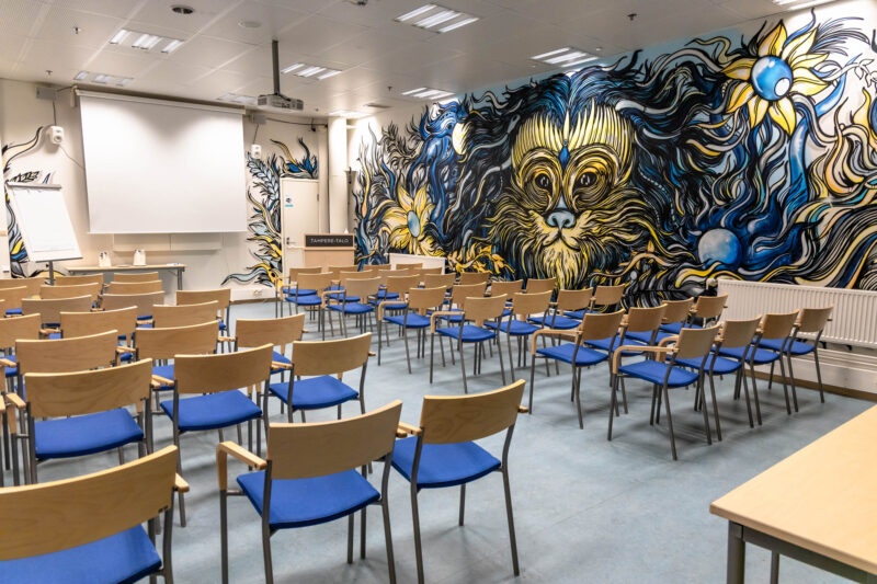 Opus 3 ovelta kuvattuna oikealla puolella kelta-sininen leijona graffiti teos ja tuolirivejä