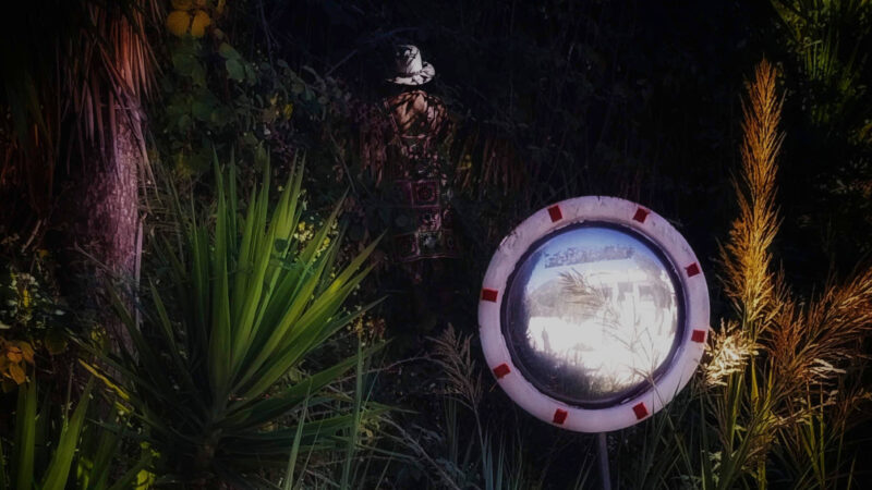 Valokuvanäytelyn teos, jossa on tumma metsäinen miljöö, peili etualalla ja ihmishahmo taka-alalla.